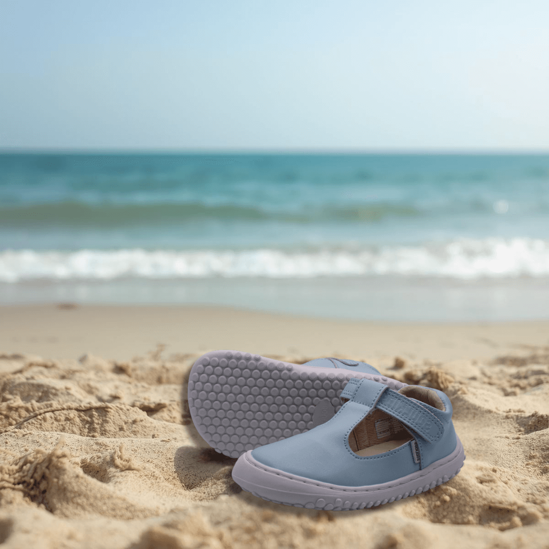 Zapato ergonomico barefoot Guillermina Celeste en la playa con el mar de fondo 